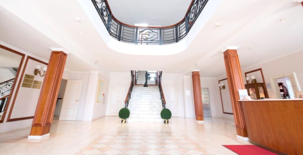 Spacious and bright foyer of Elite Clinic with chandelier, marble staircase, and reception desk