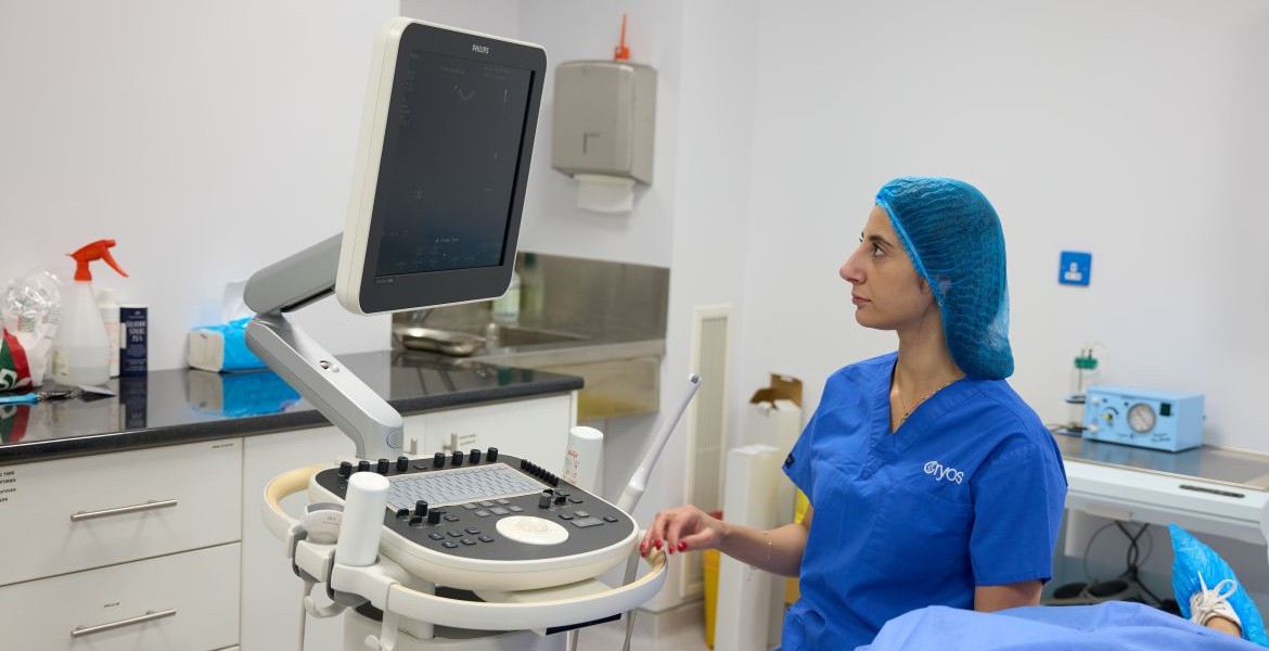 Aikaterini Rousoudiou in Cryos International IVF Clinic Cyprus performing an ultrasound scan in a medical examination room with advanced equipment.