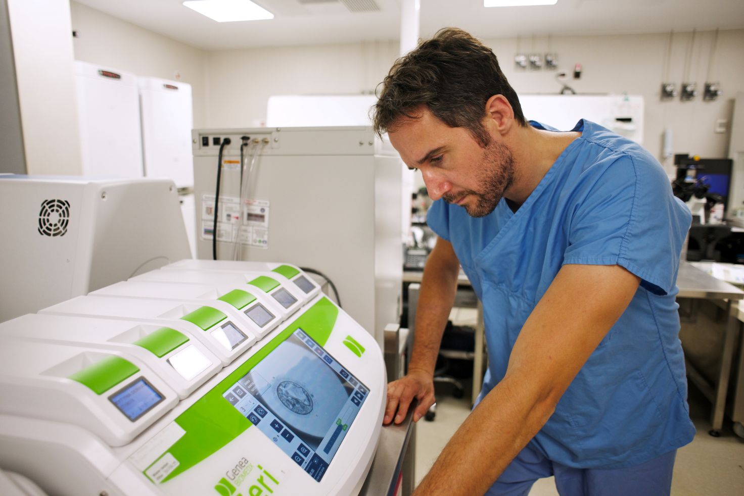 Embryologist in blue medical scrubs operating advanced fertility testing equipment at Drakopoulos IVF clinic laboratory